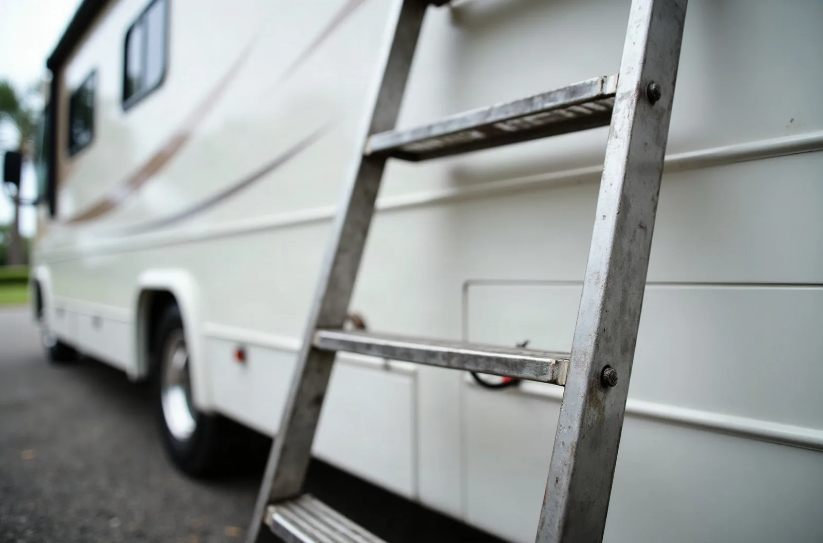 Aluminum ladder leaning against a Class A motorhome, used for accessing the roof during RV roof repair.